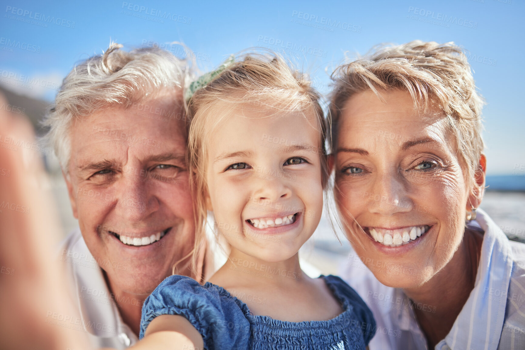 Buy stock photo Close up of little caucasian girl smiling while holding mobile phone and taking a selfie with her grandparents. Happy senior grandmother and grandfather posing for a photo with their granddaughter outdoors on a sunny day
