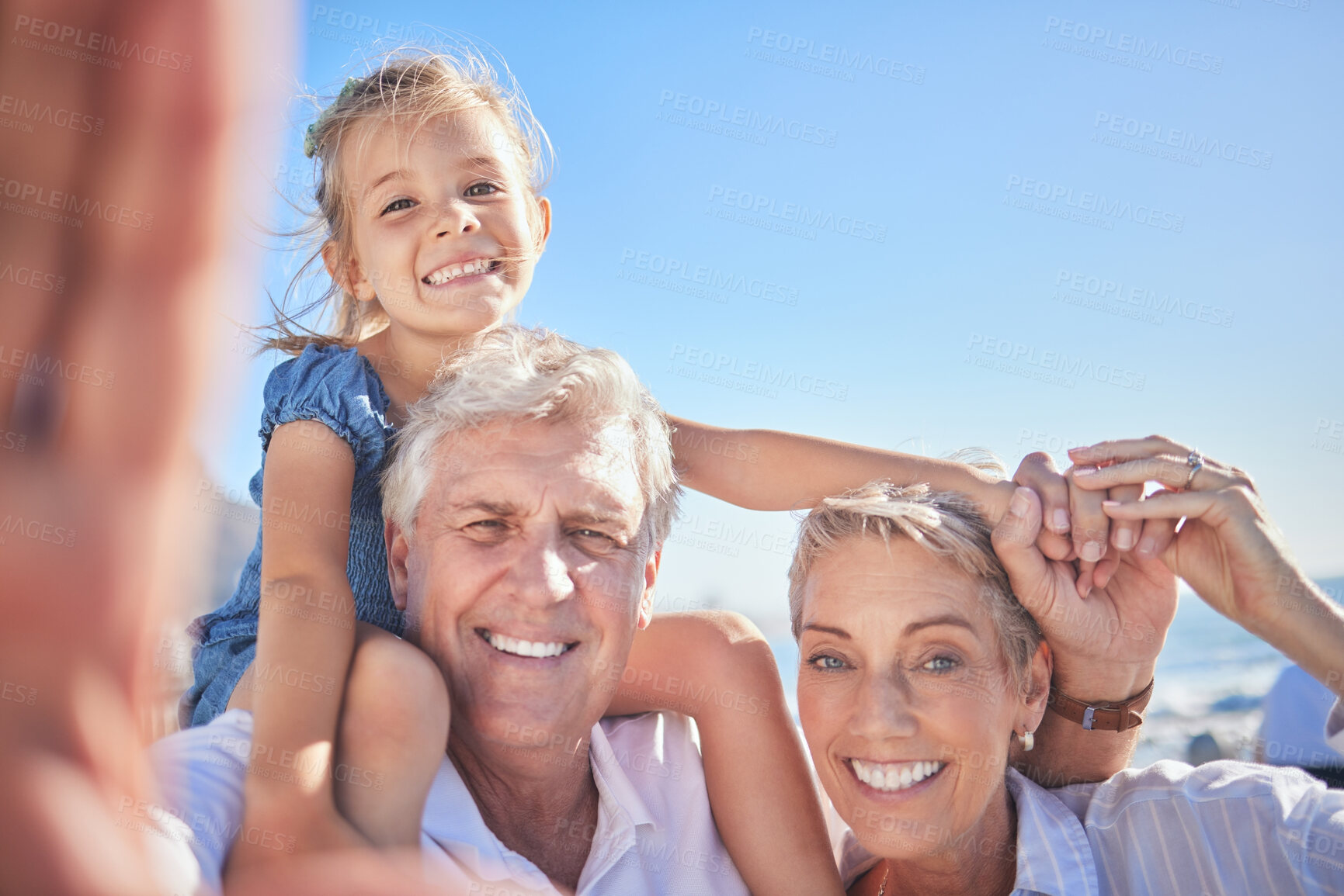Buy stock photo Loving grandparents taking a selfie while spending time with their adorable little granddaughter against a blue sky. Adorable little girl sitting on her grandfathers shoulders while her grandmother holds her hand and protects her from falling