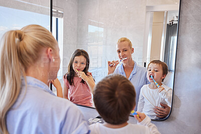 Buy stock photo Happy caucasian family using toothbrushes and looking in mirror. Young caucasian mother in pyjamas standing with her children while they brush their teeth in the bathroom at home. Little sibling brother and sister doing morning routine with mom teaching good dental hygiene