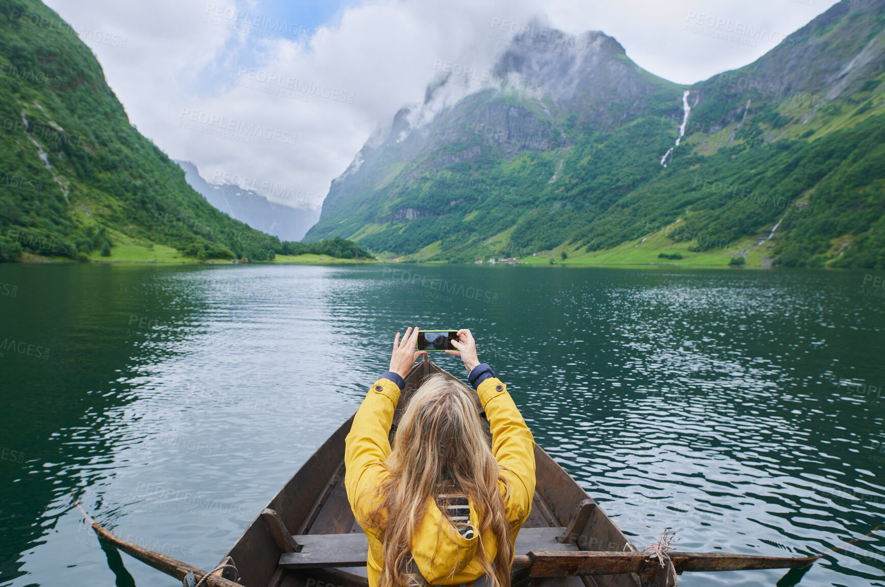 Buy stock photo Adventure woman in row boat taking photo on smart phone of beautiful fjord lake for social media