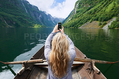 Buy stock photo Adventure woman in row boat taking photo on smart phone of beautiful fjord lake for social media