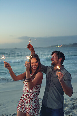 Buy stock photo happy couple holding sparklers celebrating new years eve on beach at sunset with sparkle firework