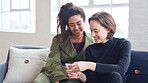 Two women friends using smartphone sitting on sofa at home browsing internet watching online entertainment on mobile phone