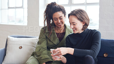 Buy stock photo Two women friends using smartphone sitting on sofa at home browsing internet watching online entertainment on mobile phone