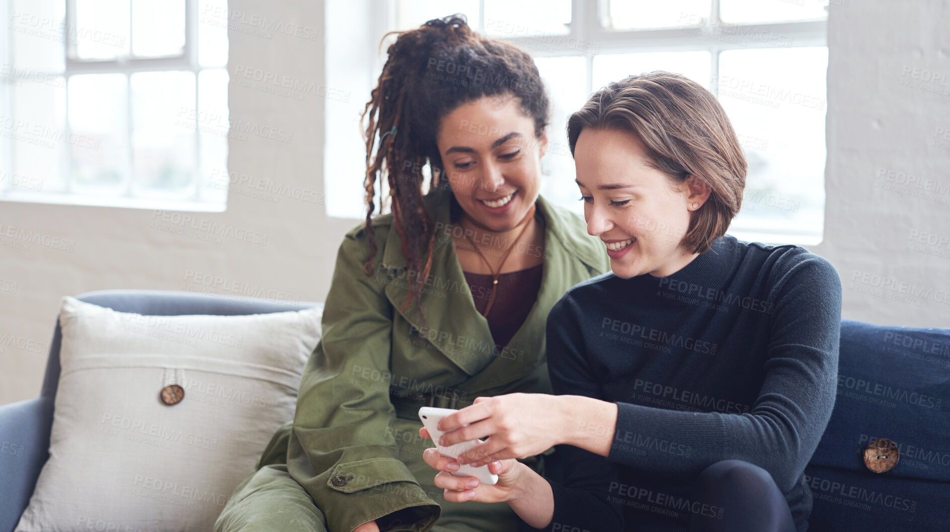 Buy stock photo Two women friends using smartphone sitting on sofa at home browsing internet watching online entertainment on mobile phone