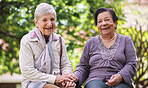 Two elderly women sitting on bench in park holding hands smiling happy life long friends enjoying retirement