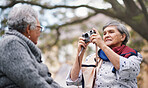 Happy old woman taking photo of friend using camera in park