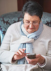 Happy elderly woman using smartphone texting browsing on mobile phone sending messages sitting on couch at home