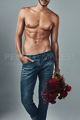Buy stock photo Studio shot of a handsome and shirtless young man holding a bunch of roses against a grey background