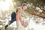 Excited little caucasian boy having fun with his grandfather as he lifts him up while playing outdoors. Active senior man playing with energetic grandson at park