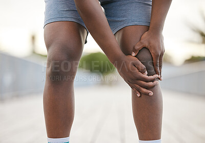 Buy stock photo A man grabbing his knee in pain from exercising. An African American jogger is bending over, grabbing his knee in pain