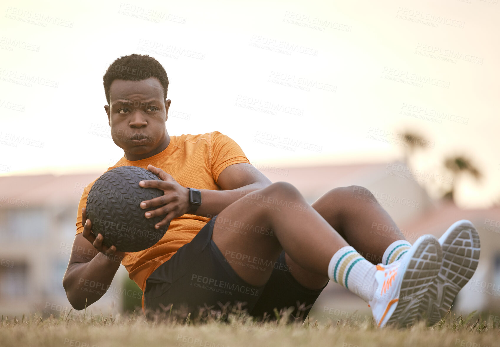 Buy stock photo A sporty man exercising, working on his fitness. An african american male athlete using a medicine ball, living an active, healthy lifestyle, sitting on the grass doing sit ups