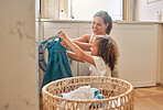 Young hispanic mother and her daughter sorting dirty laundry in the washing machine at home. Adorable little girl helping her mother with household chores