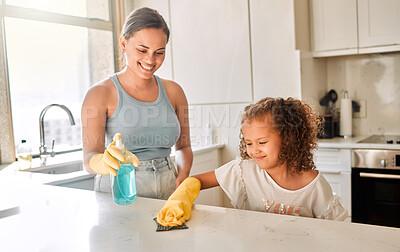 Little girl helping her mother with household chores at home. Happy mom and daughter wearing gloves while spraying and scrubbing the kitchen counter together. Kid learning to be responsible by doing tasks