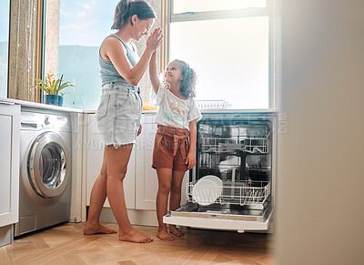 Little girl helping her mother with household chores at home. Happy mom and daughter giving high five while unloading the dishwasher together. Kid learning to be responsible by doing tasks