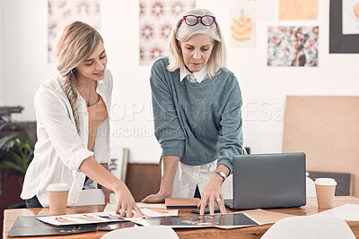 Buy stock photo Two caucasian businesswomen talking and looking at a document together at work. Female businesspeople having a meeting at a table together. Businesspeople planning and discussing a strategy
