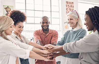 Group of five diverse businesspeople piling their hands together in an office at work. Business professionals having fun standing with their hands stacked for motivation and unity