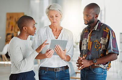 Buy stock photo Three focused businesspeople using a digital tablet together at work. Mature caucasian businesswoman talking and showing her african american coworkers an idea of a digital tablet in an office