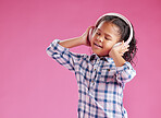 A pretty little mixed race girl with curly hair listening to music while wearing headphones against a pink copyspace background in a studio. African child singing to a song