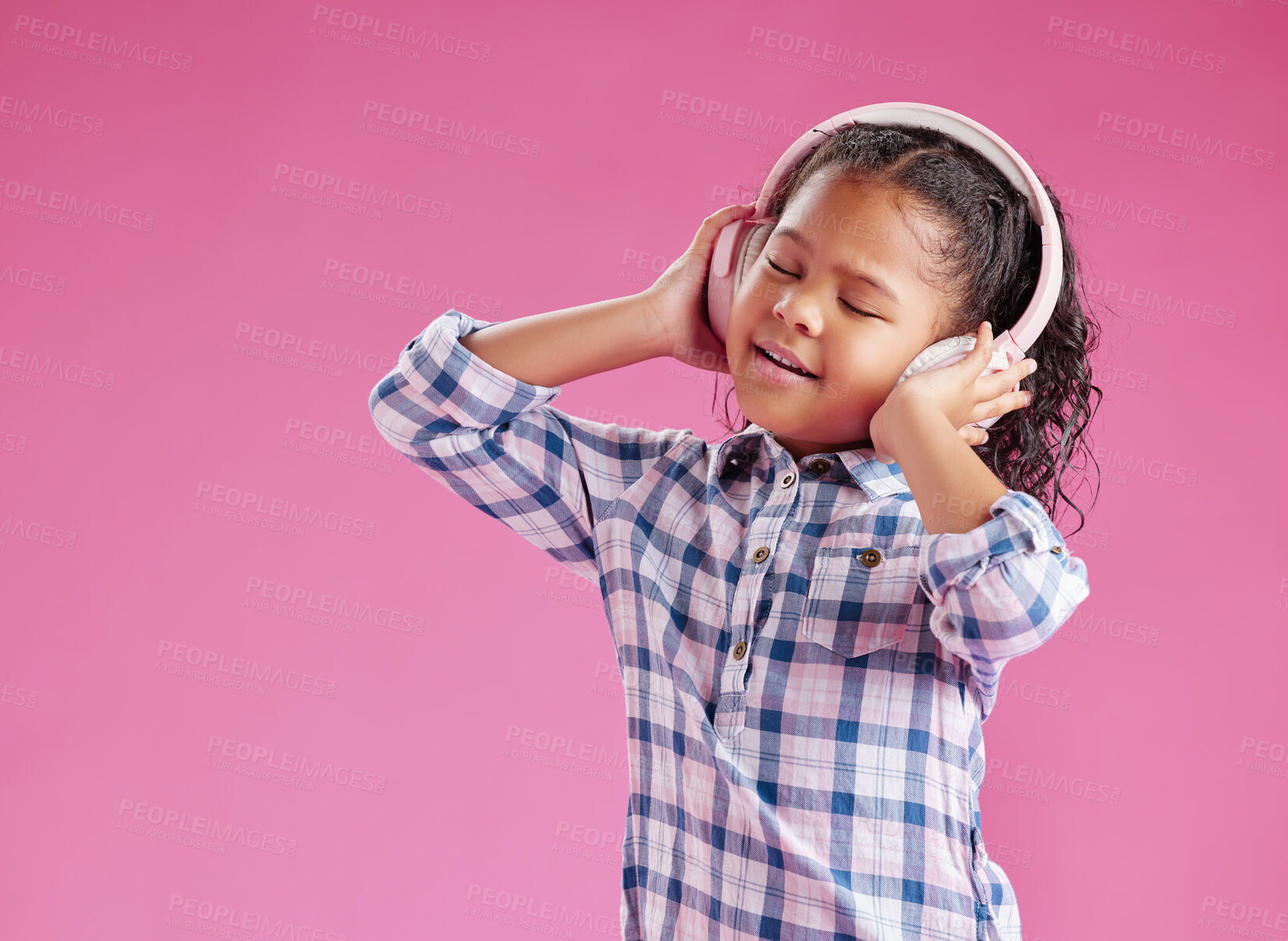 Buy stock photo A pretty little mixed race girl with curly hair listening to music while wearing headphones against a pink copyspace background in a studio. African child singing to a song
