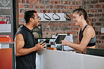 Asian man joining gym on digital tablet as member with caucasian trainer. Young coach helping, pointing and showing plan on technology. Two active fit people standing together in healthy fitness club