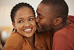 Loving young african american man kissing his wife on the cheek while she smiles and looks away. Happy young man and woman sharing romantic intimate moment at home