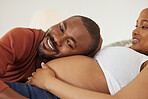 Happy young african american father to be listening to his pregnant wife’s belly and smiling. Young man putting his head against his expectant wife’s tummy listening for movement