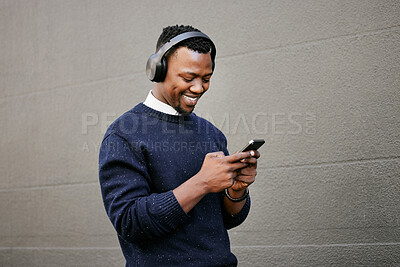 African american male using a phone while listening to music with wireless headphones outside a building during the day while smiling Young black male talking on a phone while commuting to work