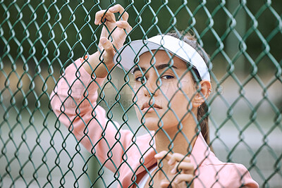 Buy stock photo Close up of a female athlete leaning against a wire fence. Young hispanic tennis player posing on a tennis court wearing a white visor and pink jacket