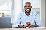 Portrait of a young happy african american businessman sitting at a desk in an office alone at work. One male businessperson smiling while using a laptop at a table at work