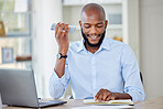 Young african american businessman on a call using a phone while reading a note in a notebook and working on a laptop in an office at work alone. One male business professional talking on a cellphone while working