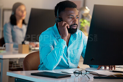 Buy stock photo One young african american call centre telemarketing agent talking on a headset while working on a computer in an office. Focused businessman consultant operating a helpdesk for customer service support