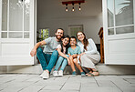 Happy young caucasian family of four sitting at their front door smiling and looking at the camera. Two parents sitting with their little son and daughter in front of their house