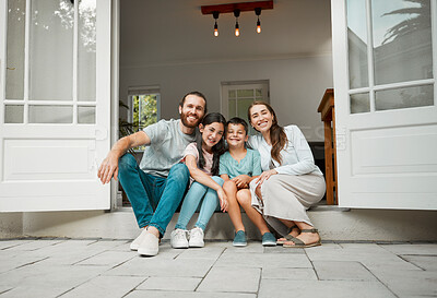 Happy young caucasian family of four sitting at their front door smiling and looking at the camera. Two parents sitting with their little son and daughter in front of their house