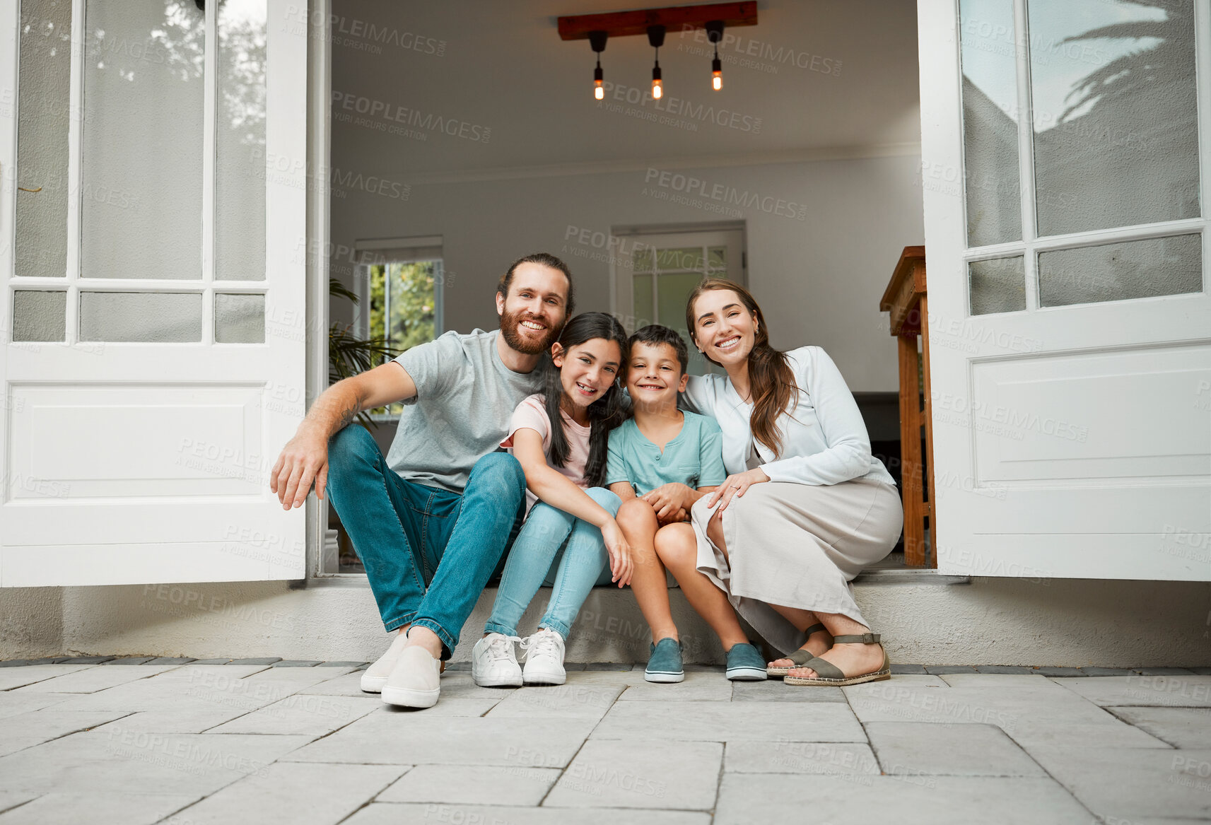 Buy stock photo Happy young caucasian family of four sitting at their front door smiling and looking at the camera. Two parents sitting with their little son and daughter in front of their house