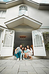 Happy young caucasian family of four sitting at their front door smiling and looking at the camera. Two parents sitting with their little son and daughter in front of their house with two big white doors