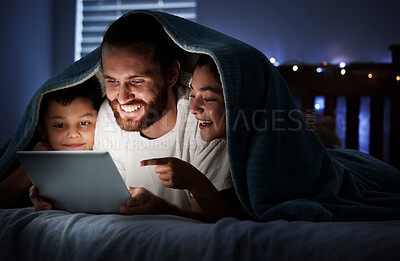 Happy caucasian family single dad with two children using digital tablet lying under blanket in the dark at night with their faces illuminated by device screen light. Father reading online story or watching video with daughter and son at night