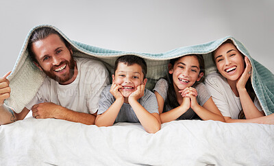 Portrait of happy caucasian family of four lying together on bed with a sherpa blanket over their heads. Carefree parents spending free time with their daughter and son over the weekend. Smiling family staying in bed and enjoying a lazy morning