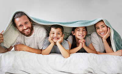 Portrait of happy caucasian family of four lying in a row on a bed with a fleece blanket over their heads. Carefree parents spending free time with their daughter and son over the weekend. Smiling family staying in bed and enjoying a lazy morning