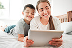 Happy caucasian mother and son holding digital tablet while lying together on a bed. Little boy and mom watching movie online or playing game while spending time at home