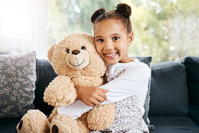 Portrait of an adorable little hispanic girl holding a teddy bear at home. Cute mixed race girl playing with her toy while sitting on the couch in the lounge