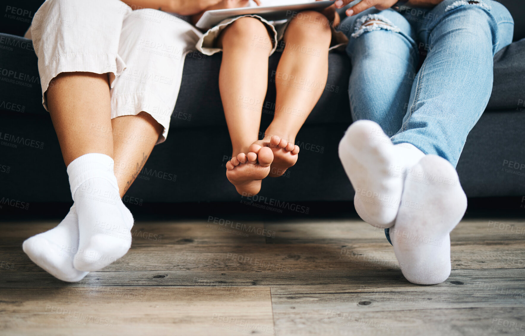 Buy stock photo Closeup of a family sitting on a sofa using a tablet in the lounge at home. Family feet relaxing while sitting on a couch during the day