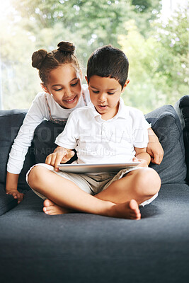 Buy stock photo Closeup of a mixed race brother and sister playing together using their digital tablet on the sofa at home. Hispanic cute little boy and girl using a wireless device while sitting on the couch in the lounge