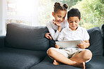 Closeup of a mixed race brother and sister playing together using their digital tablet on the sofa at home. Hispanic cute little boy and girl using a wireless device while sitting on the couch in the lounge