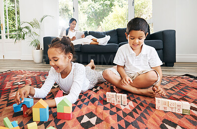 Buy stock photo Little kids sitting on the floor with toys and colouring in a book. Small mixed race brother and sister playing together at home while parents sit in the background