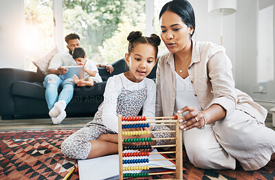 Hispanic mother sitting on the floor in the lunge at home smiling with her daughter while playing with educational toys. Adorable little girl playing while bonding and spending time with her mom at home while using a abacus to help her kid co