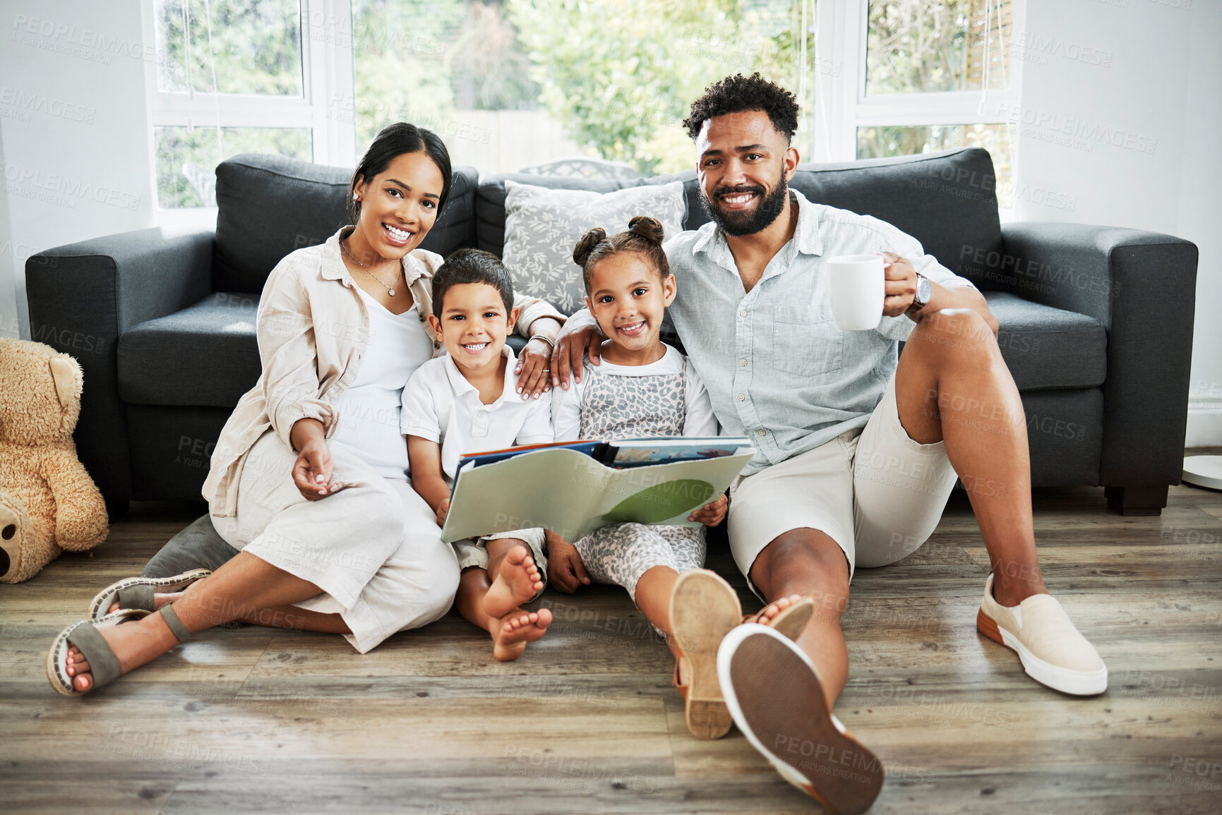 Buy stock photo Mixed race family reading a book together on the floor at home. Hispanic mother and father teaching their little son and daughter how to read. Brother and sister learning to read with their parents