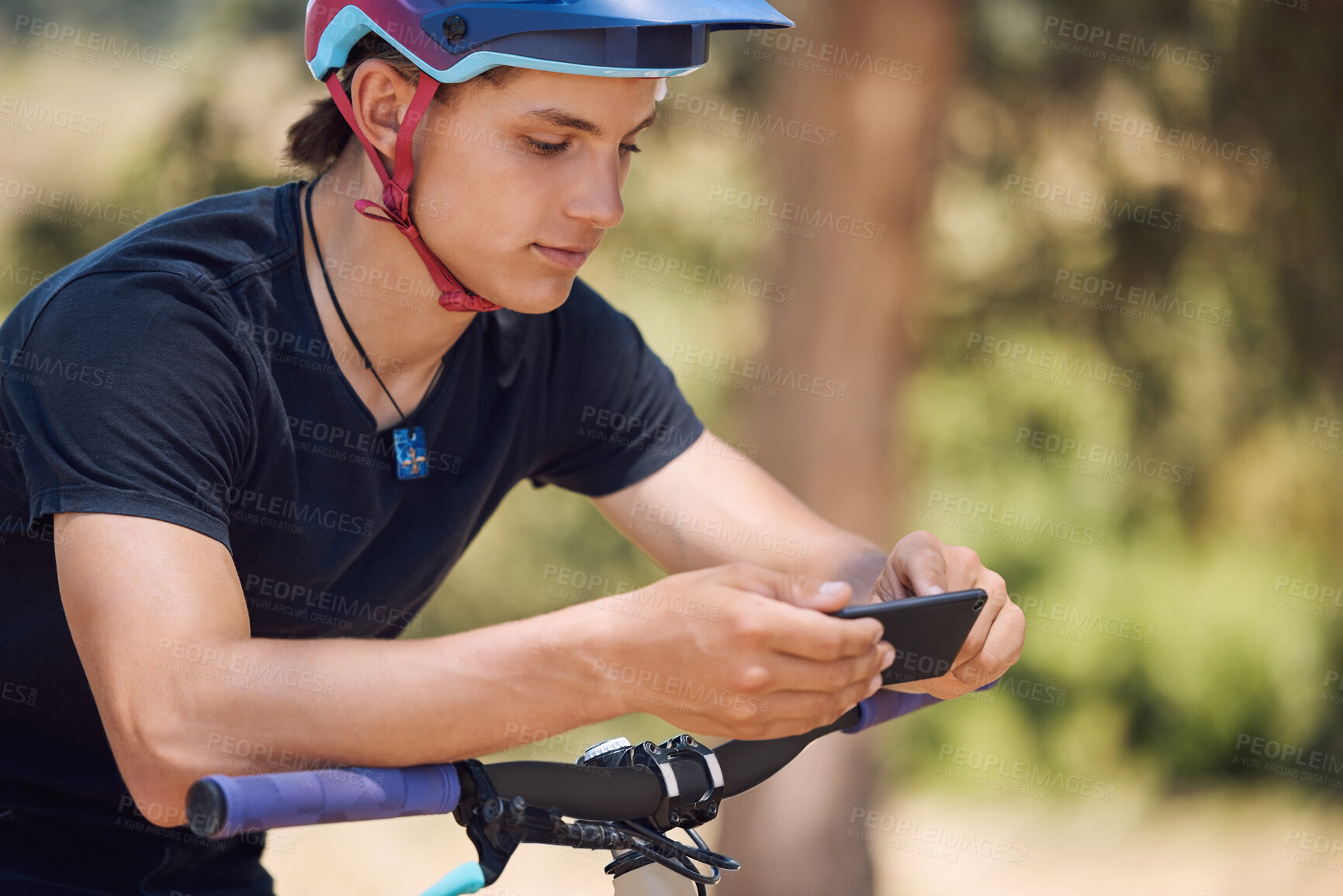 Buy stock photo Young male cyclist using a cellphone while taking a break from cycling on a bicycle. Man stopping to text and scroll social media while exercising in a park. Checking his messages before his workout