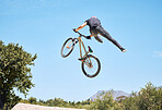 Man showing his cycling skills while out cycling on a bicycle outside. Adrenaline junkie practicing a dirt jump outdoors. Male wearing a helmet doing tricks. Unrecognizable passionate guy having fun