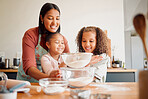 Females only, happy mixed race family of three cooking in a messy kitchen together. Loving black single parent bonding with her daughters while teaching them domestic skills at home